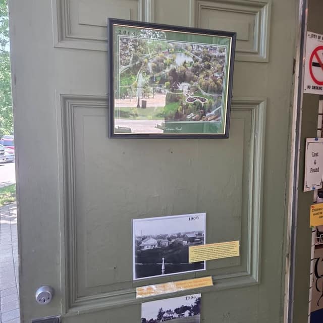 A green door displays a framed aerial picture of Victoria Park dated 2008 and black-and-white photos dated 1906 and 1996 with notes.