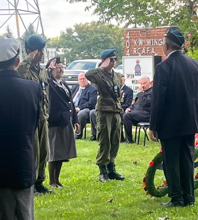 Cadets and veterans in berets salute on a lawn outside the 404 K-W Wing R.C.A.F. sign while seated guests look on.