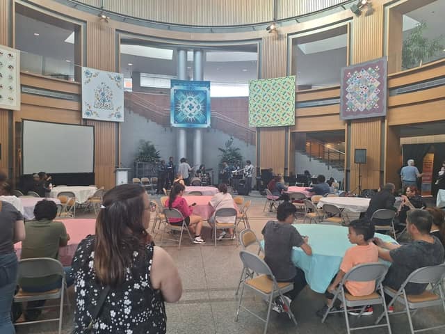 Families sit at round tables in an atrium as a band plays on a small stage beneath large hanging quilts.