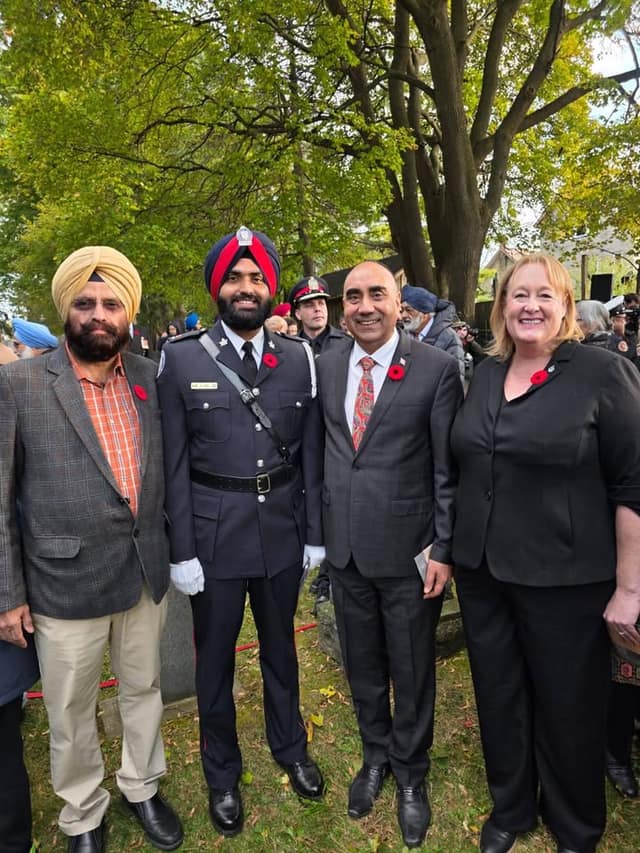 A woman and a man in a suit pose with a man in a tan turban and an officer in a navy turban and dress uniform, all wearing poppies.