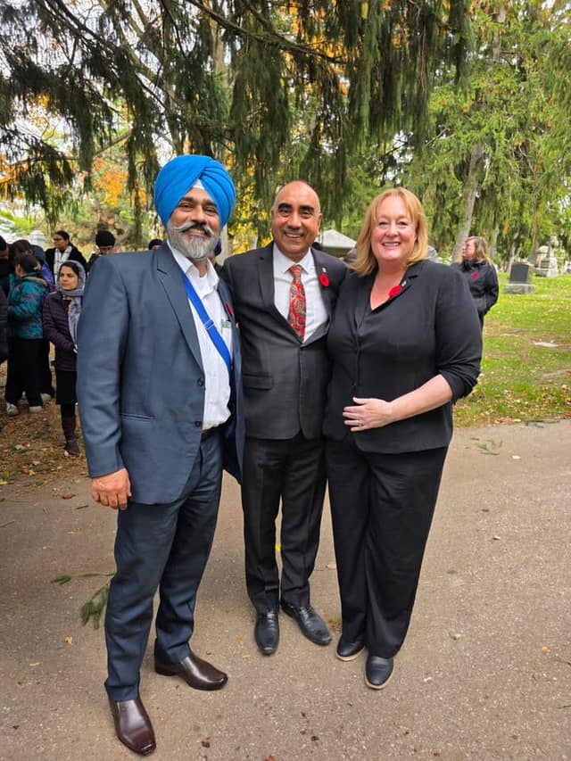 A man in a blue turban and blazer, a man in a gray suit and a woman in black pose smiling on a cemetery path.
