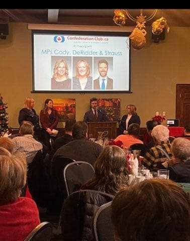 Three speakers stand at a podium beside a screen reading "Confederation Club.ca" and "MPs Cody, DeRidder & Strauss" as seated guests watch.
