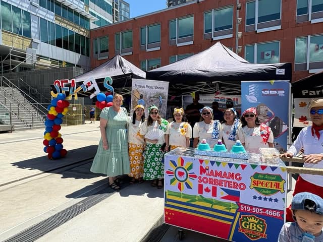 A woman in a green dress stands with six women in Filipino-style dress behind a Mamang Sorbetero ice cream cart, beside a balloon arch.