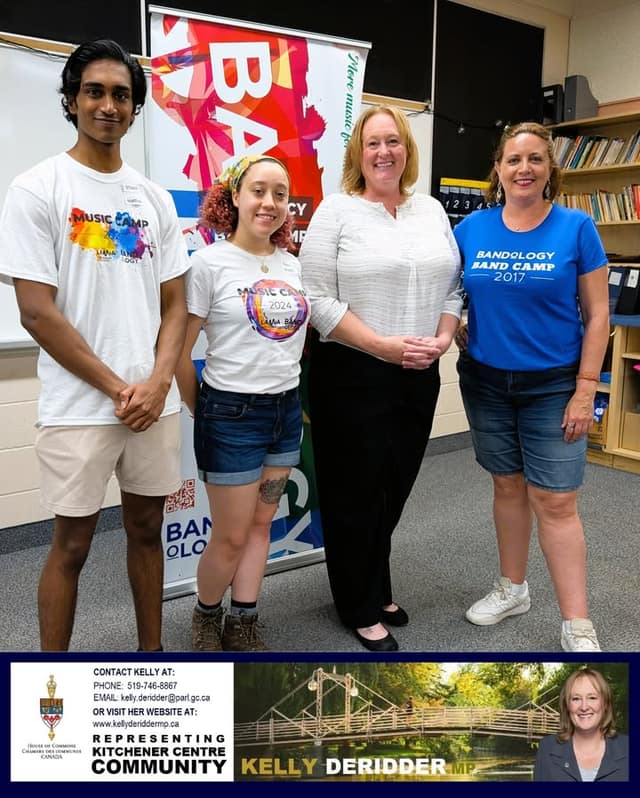 Four people pose in a classroom in front of a Bandology banner, two in Music Camp shirts, one in a blue Bandology Band Camp 2017 shirt.
