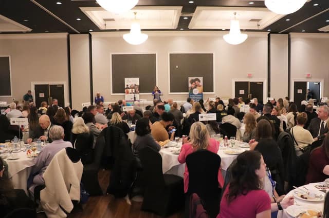 A large ballroom full of guests seated at round tables, with a speaker at the front between two Child Witness Centre banners.