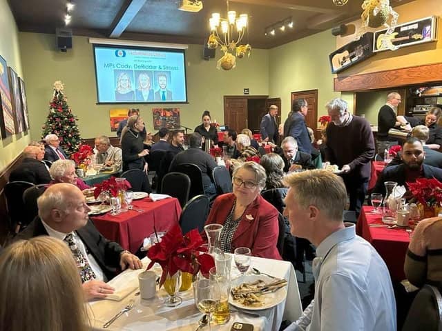 Guests sit at tables with red cloths and poinsettias in a banquet room while a screen reads "MPs Cody, DeRidder & Strauss".
