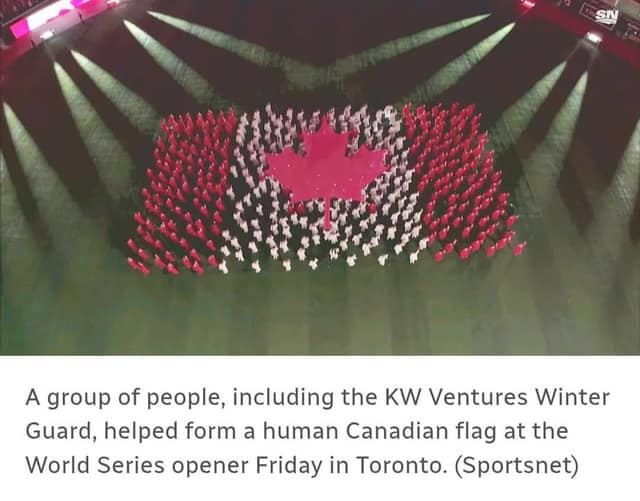 Aerial view of people in red and white outfits forming a human Canadian flag with a maple leaf on a field under spotlights.