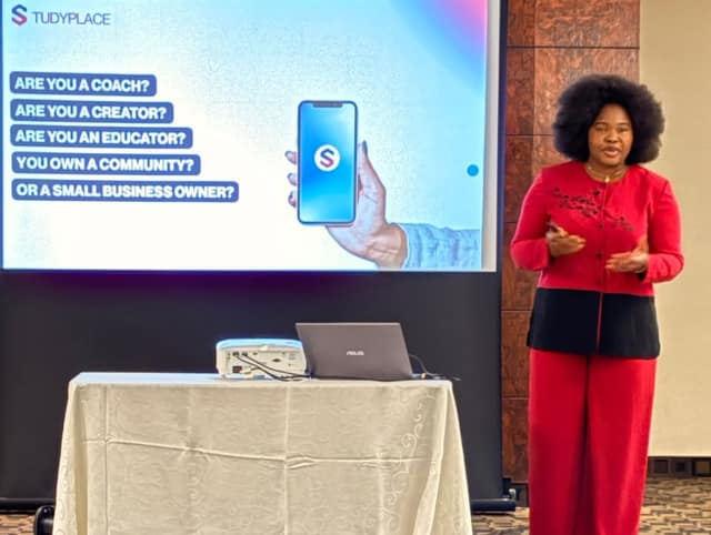 A woman in a red outfit presents beside a projector screen reading "Are you a coach? Are you a creator? Are you an educator?"