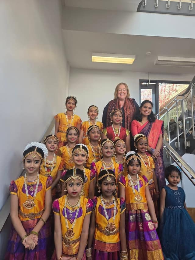 Young girls in gold and purple dance costumes and jewelry pose on a staircase with two smiling women standing behind them.