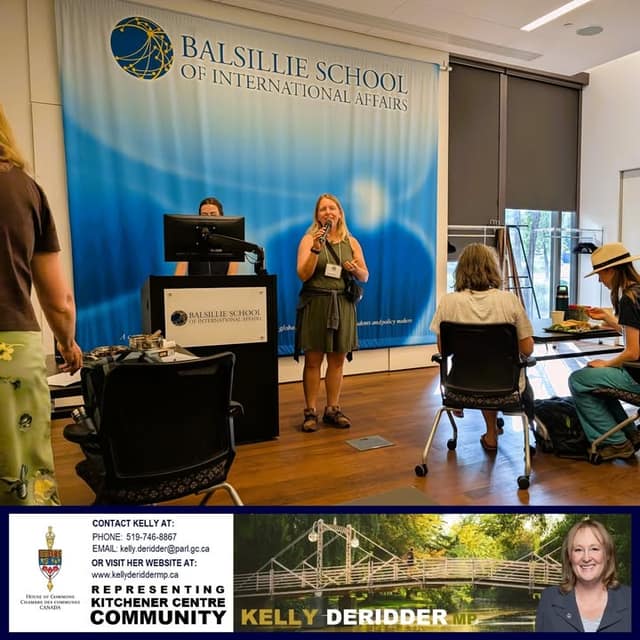 A woman with a microphone speaks beside a podium in front of a Balsillie School of International Affairs banner as guests sit nearby.