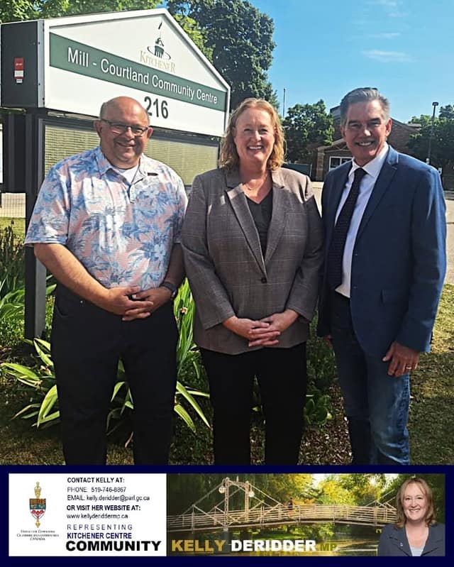 Two men and a woman in the middle stand smiling in front of the Mill - Courtland Community Centre sign, with plants and trees behind.