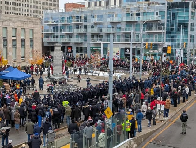 Seen from above, a large crowd fills a downtown square around a cenotaph as uniformed ranks and a band stand in formation.