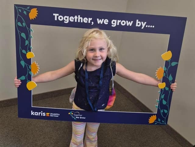 A smiling young girl with blonde hair holds a blue photo frame reading "Together, we grow by...." with Karis logos.
