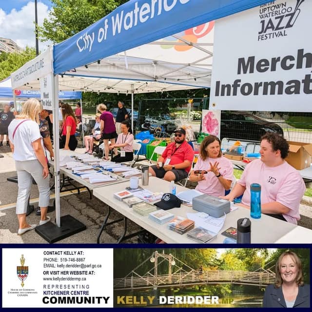 Volunteers sit and stand at tables of printed materials under a City of Waterloo tent near an Uptown Waterloo Jazz Festival merchandise sign.