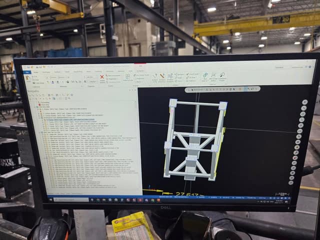 A computer monitor showing CAD/CAM software with a list of machining toolpaths and a 3D model of a steel frame.