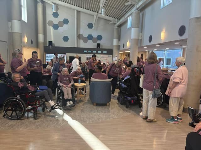 Residents in wheelchairs and people in purple Walk to Wellness shirts gather inside a bright, high-ceilinged common room.