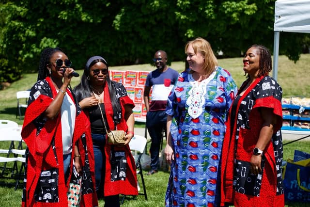 A woman speaks into a microphone beside another woman in matching red robes, as two others look on at a park event.