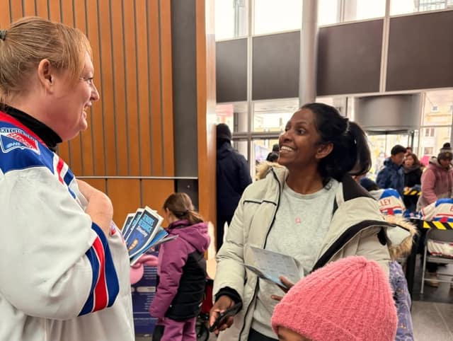 A smiling woman in a Kitchener Rangers jersey hands out Seniors Resource Directory booklets to a smiling woman in a cream winter coat.