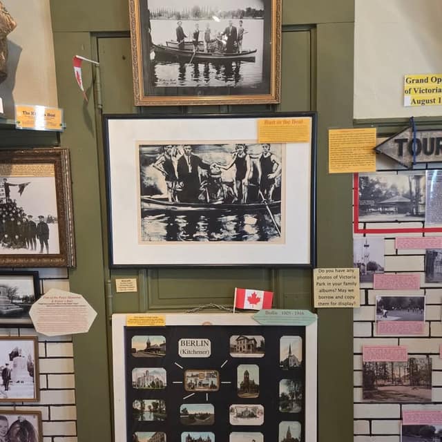 Gallery wall with framed black-and-white photos of men in a rowboat, a Canadian flag, and a board of Berlin (Kitchener) postcards.