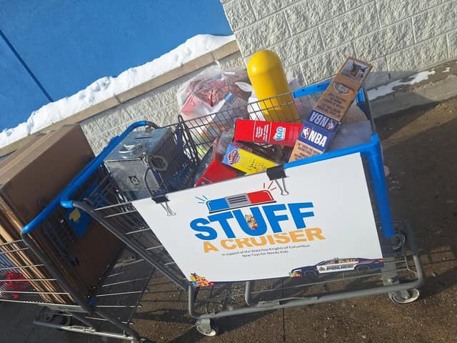 A shopping cart of donated toys, including NBA and Play-Doh boxes, with a Stuff a Cruiser sign for the Waterloo Knights of Columbus.