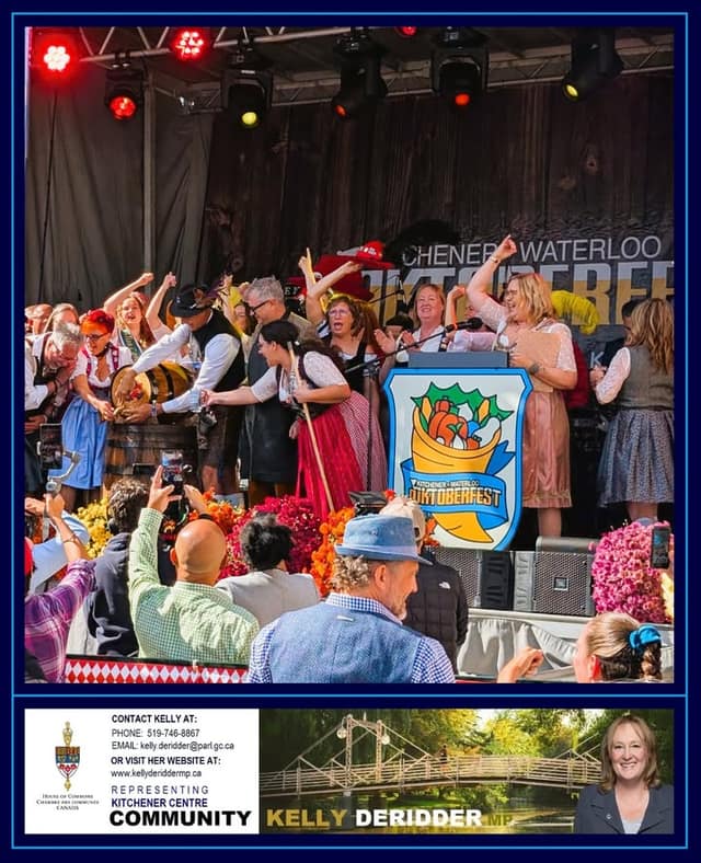 People in Bavarian dress cheer on a decorated stage with a wooden keg and a podium bearing a Kitchener-Waterloo Oktoberfest sign.