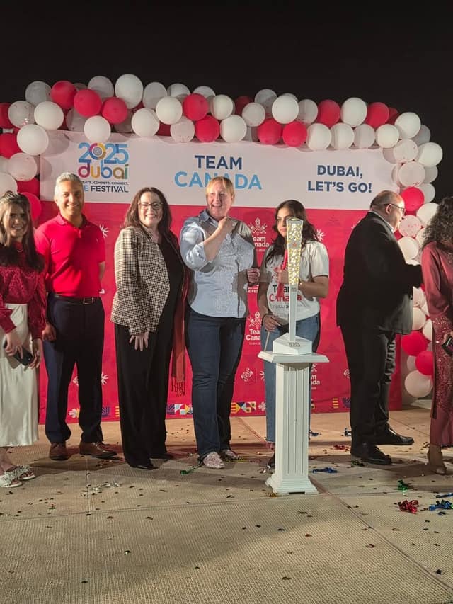 Five adults and a young woman stand on stage beside a white pedestal with a glowing lantern, in front of the Team Canada backdrop.