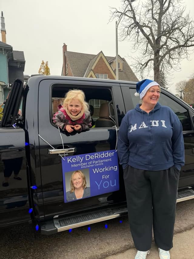 A smiling child leans out of a black pickup window beside a woman in a blue hat; a sign reads "Kelly DeRidder, Member of Parliament."