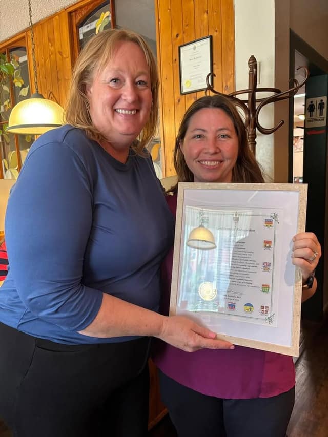 Two smiling women stand inside a restaurant holding a framed Certificate of Recognition for Metro Restaurant.