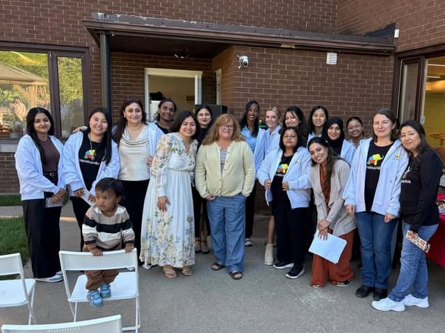 A large group of smiling staff in Marvelous Minds shirts and light jackets pose outdoors by a brick building, with a toddler in front.