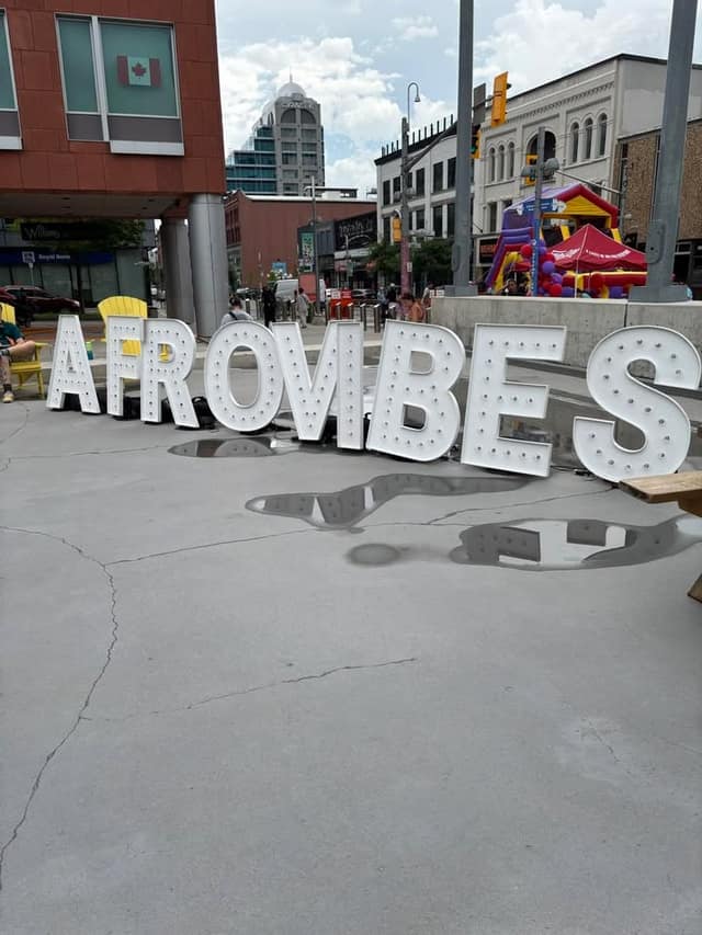 Large white marquee letters spelling AFROVIBES stand on a plaza, with puddles on the ground and a bouncy castle behind.