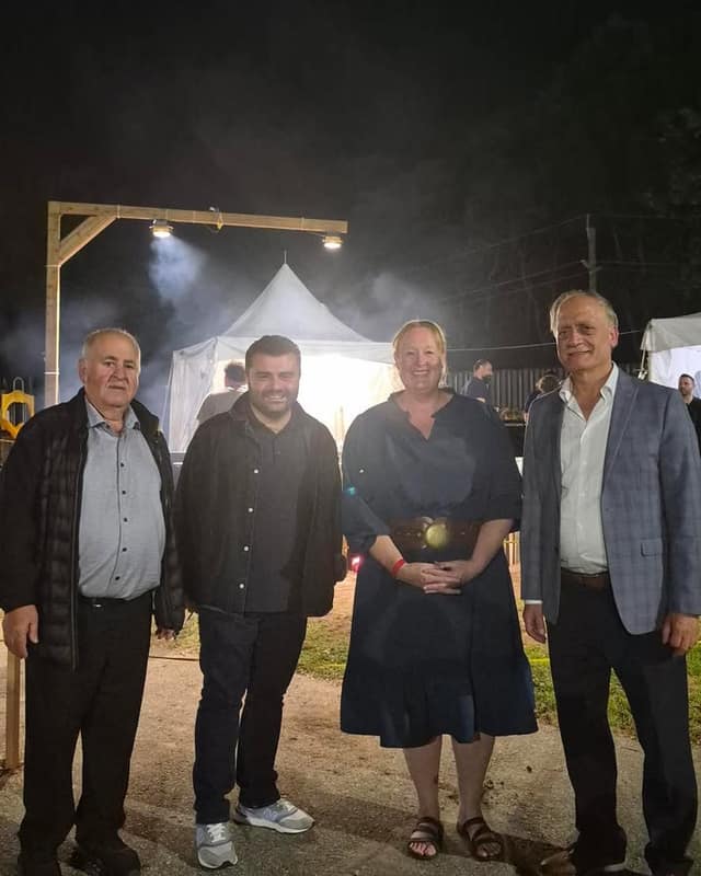 Four people stand smiling side by side outdoors at night in front of a lit white tent and a wooden frame with floodlights.