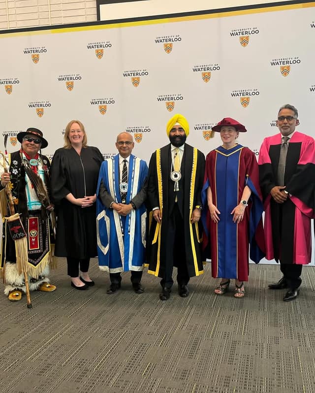 Six people in academic and ceremonial regalia, including one in a black gown, stand in a row before a University of Waterloo backdrop.