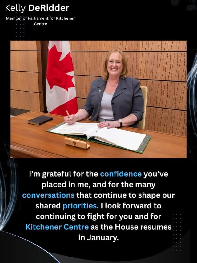 Kelly DeRidder smiles at a wooden desk, pen in hand, signing a large open book beside a Canadian flag.