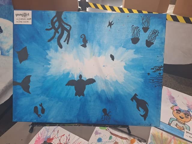 Painting of black silhouettes of a sea turtle, jellyfish, stingray, seahorse and octopus on a blue ocean background with a young@art label.