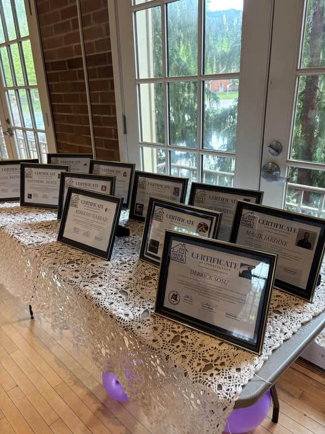 Framed Gigi's House certificates of appreciation, including ones for Derrick Sosu and Malik Jardine, sit on a lace-covered table by windows.