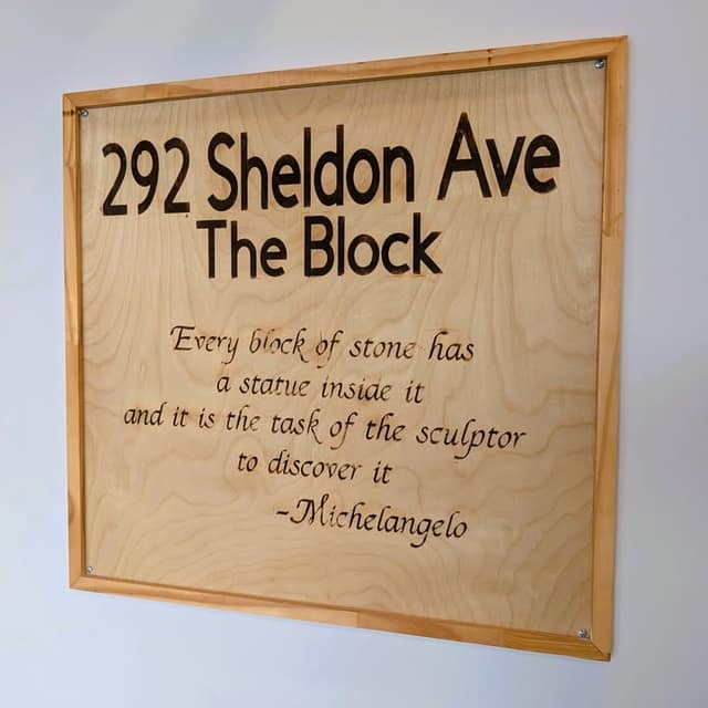 Wooden framed sign reading "292 Sheldon Ave, The Block" with a Michelangelo quote about every block of stone having a statue inside it.
