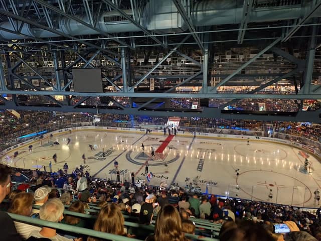 A packed arena seen from the upper seats, with players warming up on the ice and a red carpet laid out at center ice.