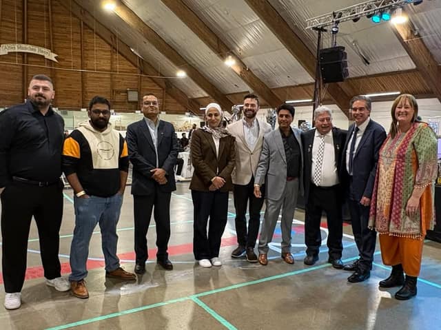 Eight people in business and casual clothing stand together on an indoor arena floor beneath a wooden-beamed ceiling.