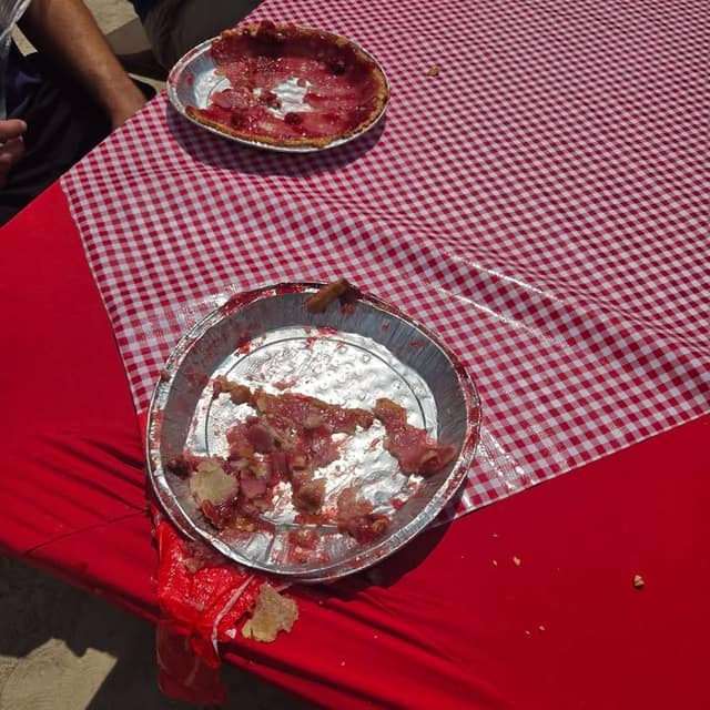 Two empty foil pie plates with cherry filling remnants and crust crumbs sit on a red and white gingham tablecloth.