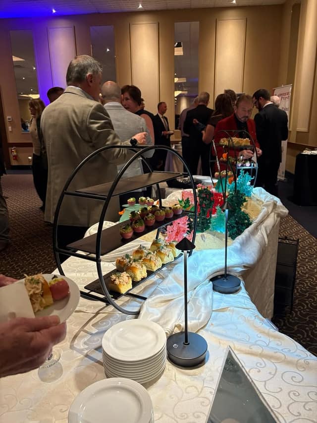 Guests mingle behind a buffet table with tiered stands of small appetizers, stacked white plates and sea-themed decorations.