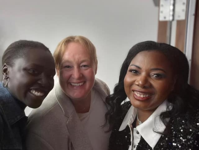 Three smiling women pose together for a selfie indoors beside a wooden door.